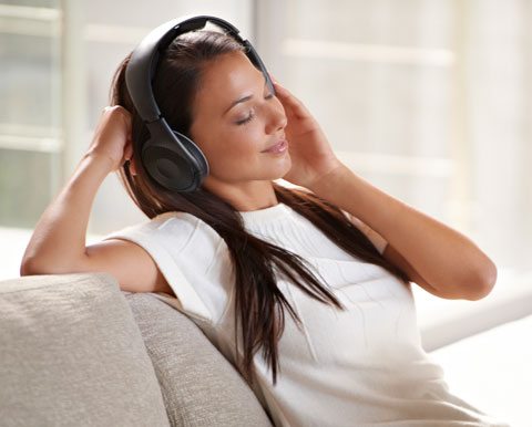 calm music, woman sitting on couch, eyes closed, listening to headphones.