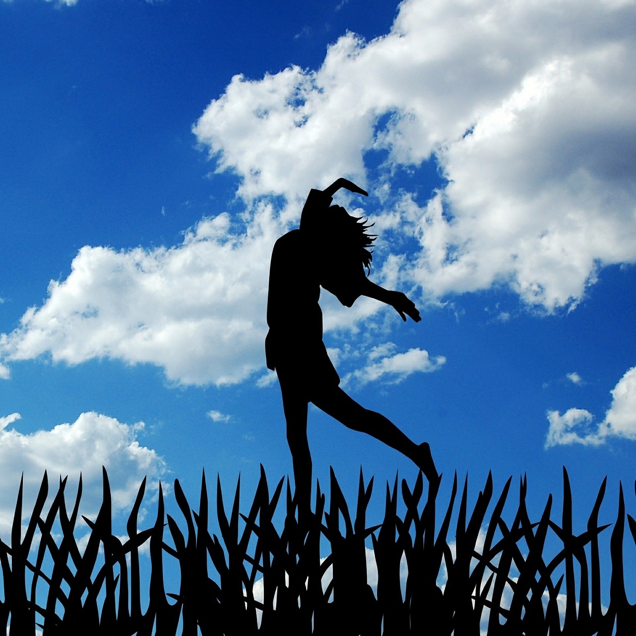 Personal growth. A female silhouette jumping with hands over head set against blue sky with clouds.