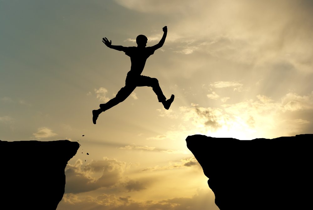 What is hypnosis? Image of a silhouette of a man jumping over crevasse backlit against sun and some clouds