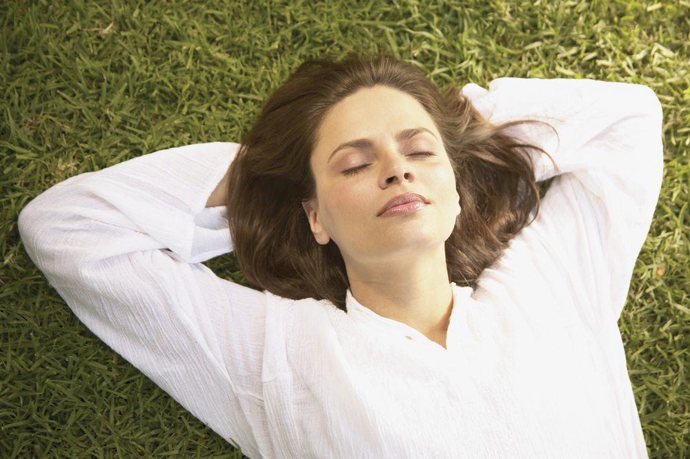What is hypnosis? Image of a women laying on grass with her eyes closed and hands behind her head.