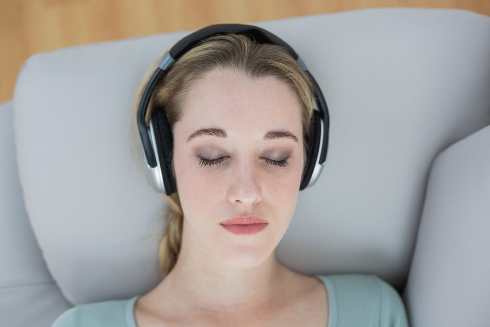 What is hypnosis? Image of a female laying back against couch arm listening with headphones and eyes closed