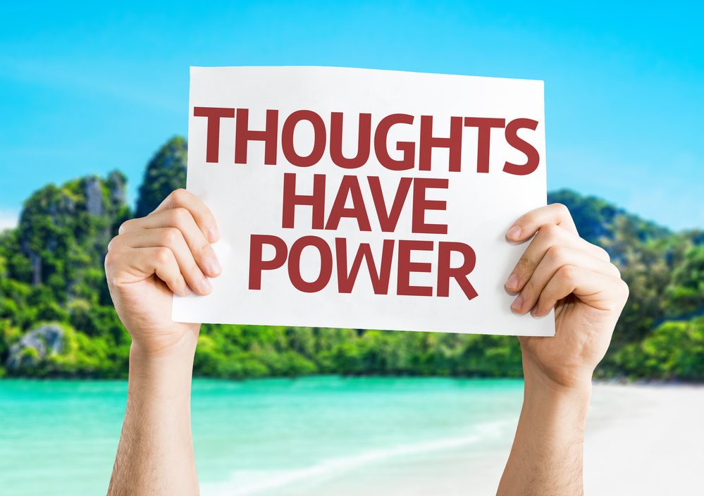 Positive affirmations hands holding up a sign that reads thoughts have power set in a tropical coastline
