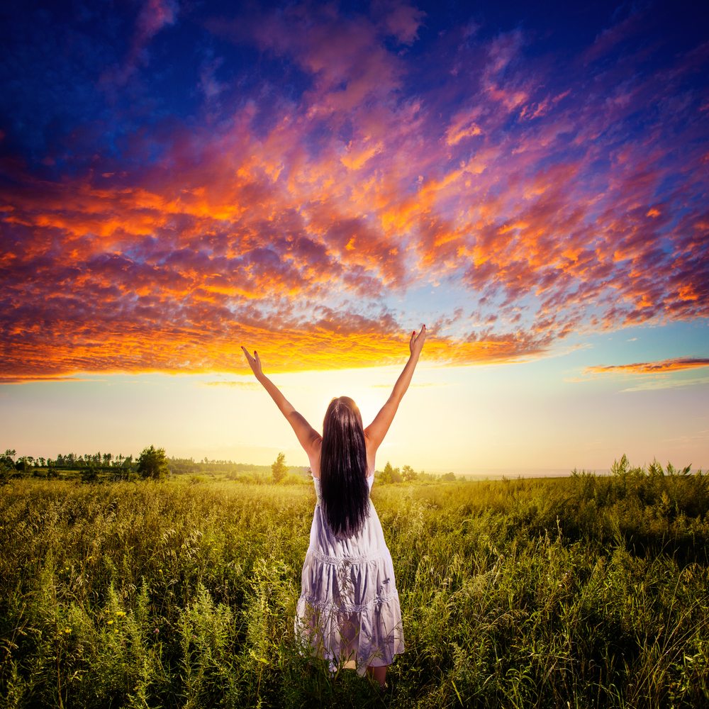 Positive affirmations a woman in a field of grass with orange and blue clouds overhead