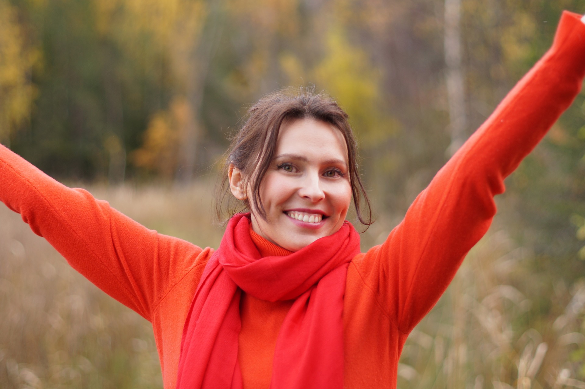 higher consciousness, smiling women with her arms out stretched overhead in a red scarf and orange sweater