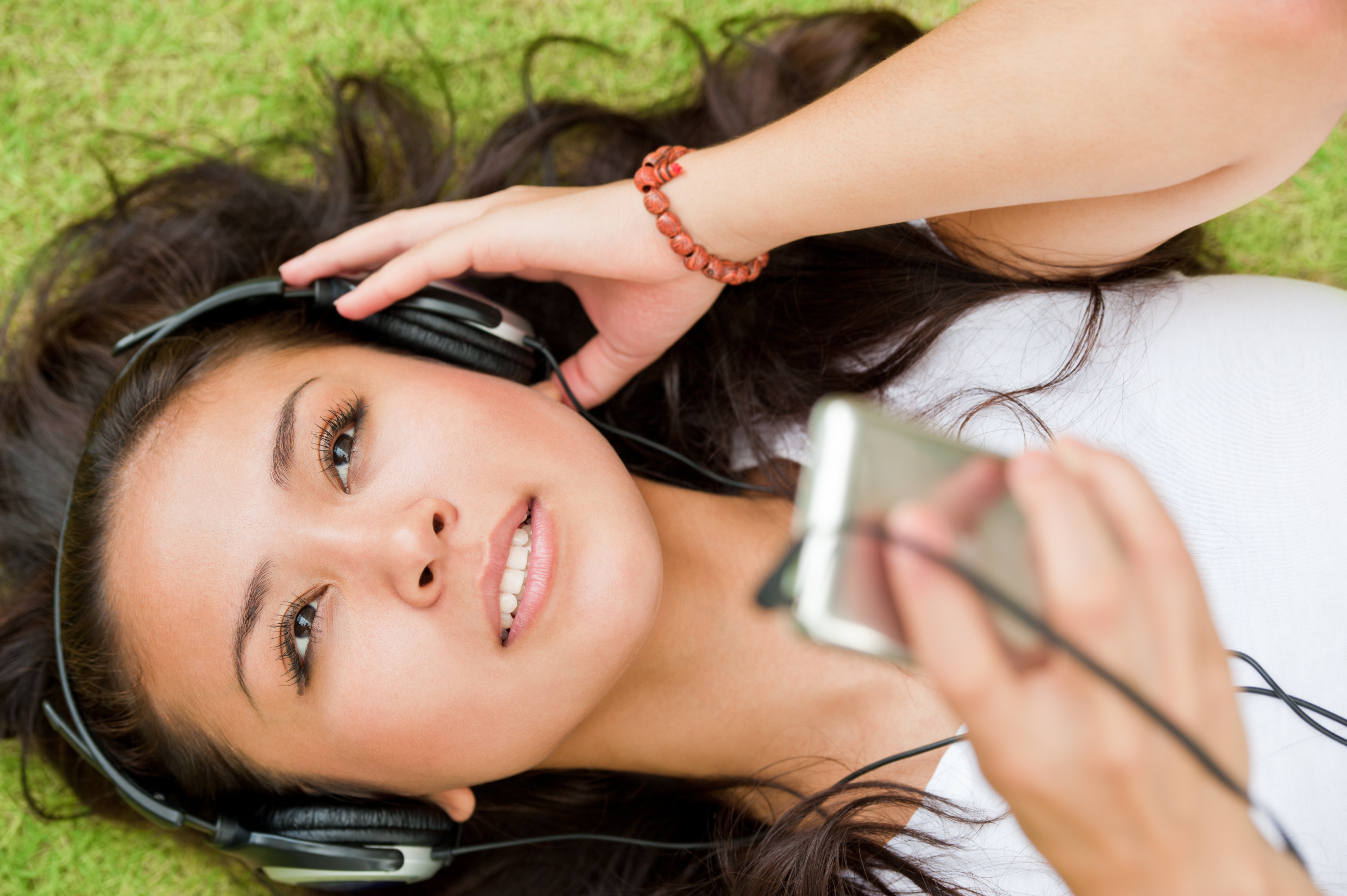Self Hypnosis Audio - A woman listening to headphones lying on her back on grass