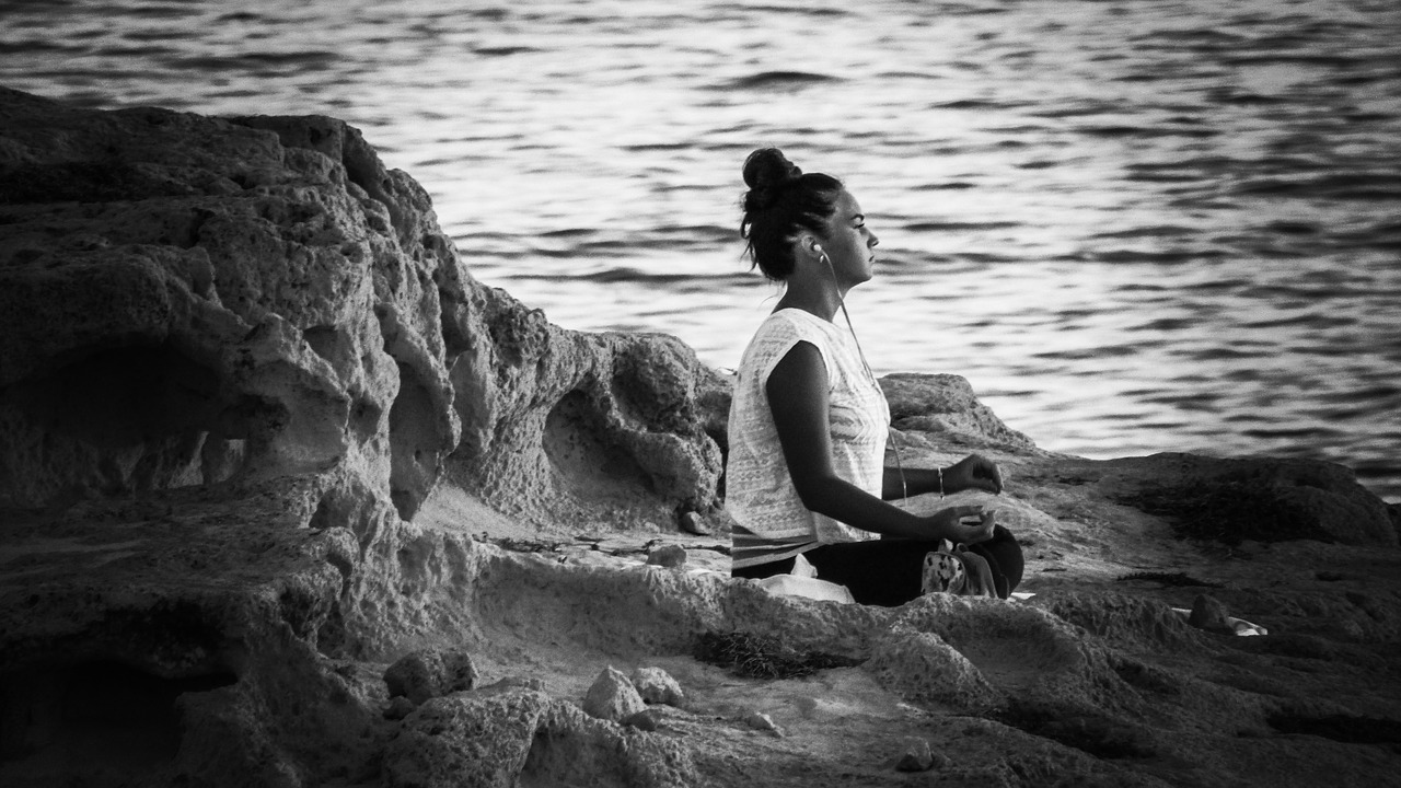 mind power techniques-black and white photo of young lady meditating with headphones on ocean bluff