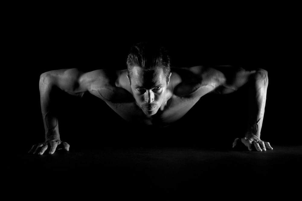 mind power techniques-Man with focused eyes doing pushups on black background