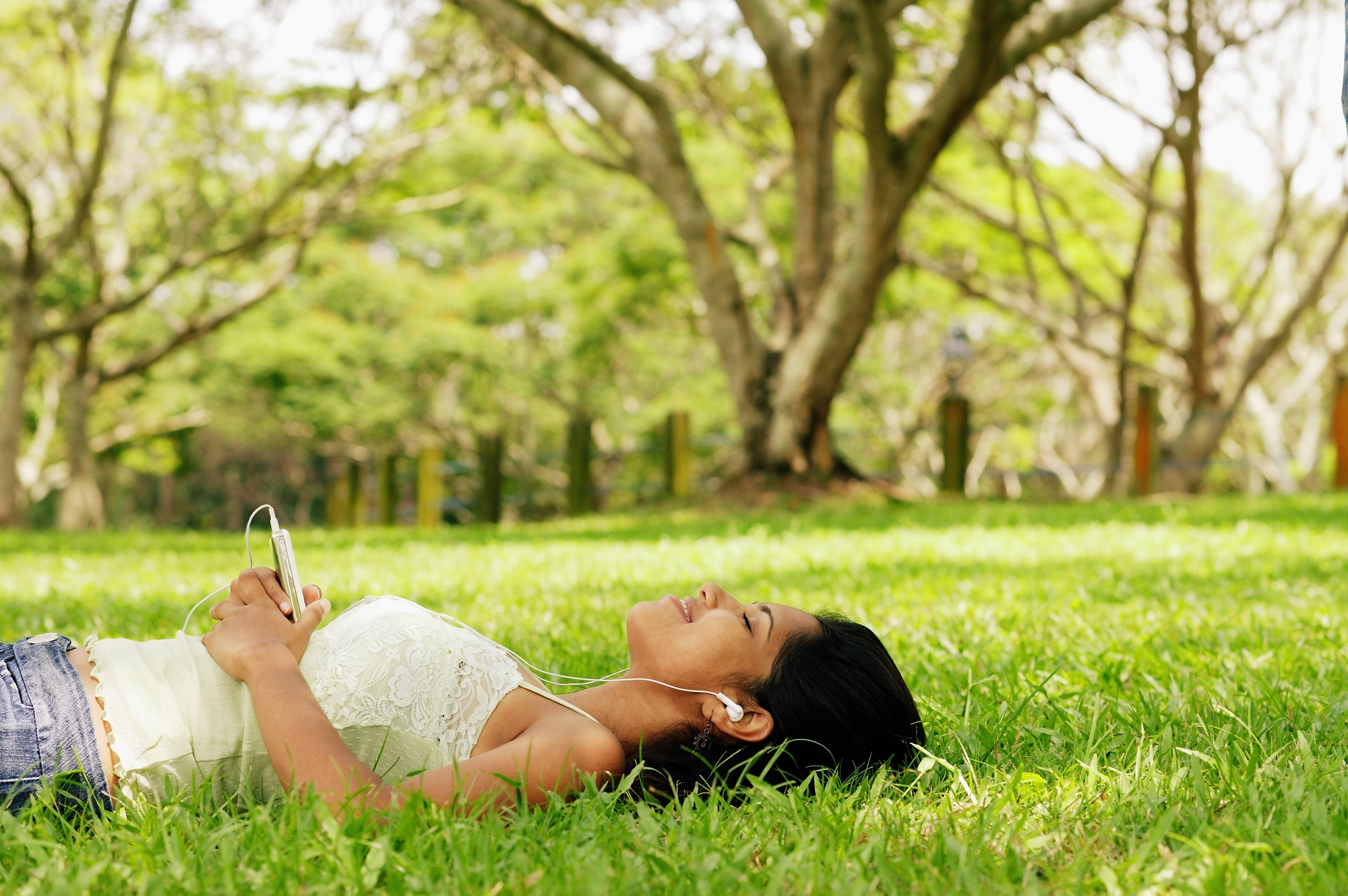 Self hypnosis for weight loss - a young woman listening to a music device with earbuds while laying on grass in a park